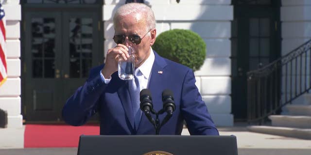 President Joe Biden drinks a glass of water during a speech.