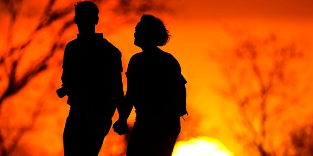 In this March 10, 2021 file photo, a couple walks through a park at sunset in Kansas City, Mo. U.S. life expectancy dropped for two consecutive years in 2020 and 2021, marking the first such trend since the early 1920s, according to a new government report. 