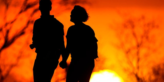 In this March 10, 2021 file photo, a couple walks through a park at sunset in Kansas City, Mo. U.S. life expectancy dropped for two consecutive years in 2020 and 2021, marking the first such trend since the early 1920s, according to a new government report.