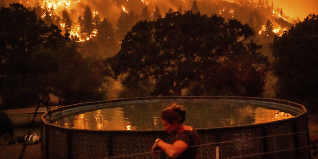 Angela Crawford leans against a fence as a wildfire called the McKinney fire burns a hillside above her home in Klamath National Forest, Calif., on Saturday, July 30.