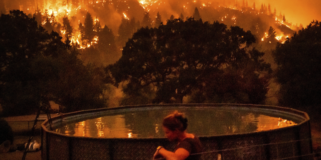 Angela Crawford leans against a fence as a wildfire called the McKinney fire burns a hillside above her home in Klamath National Forest, Calif., on Saturday, July 30.