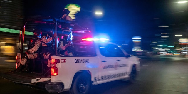 2022년 8월 12일 멕시코 바하칼리포르니아주 티후아나에서 무장한 주방위군이 신원 미상의 개인들에 의해 불에 탄 집단 수송 차량의 현장을 지나고 있다. 