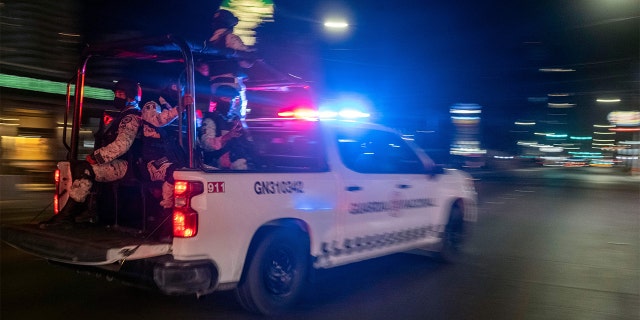 Armed members of the National Guard drive past the site of a burnt collective transport vehicle after it was set on fire by unidentified individuals in Tijuana, Baja California state, Mexico, Aug. 12, 2022. 