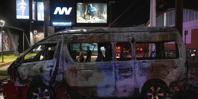 People look at a burnt collective transport vehicle after it was set on fire by unidentified individuals in Tijuana, Baja California state, Mexico, Aug. 12, 2022.