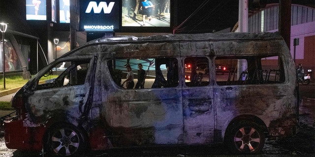 People look at a burnt collective transport vehicle after it was set on fire by unidentified individuals in Tijuana, Baja California state, Mexico, Aug. 12, 2022.