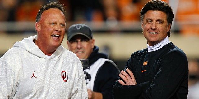 Offensive coordinator Cale Gundy of the Oklahoma Sooners jokes with his brother, head coach Mike Gundy of the Oklahoma State Cowboys, before their game at Boone Pickens Stadium on November 27, 2021 in Stillwater, Oklahoma.
