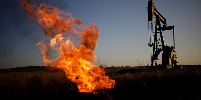 A natural gas flare burns near an oil pump jack at the New Harmony Oil Field in Grayville, Illinois, US, on Sunday, June 19, 2022.