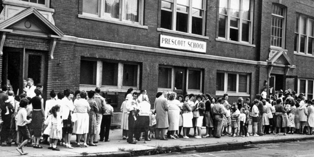 FILE - Parents and their children line up outside a Syracuse school to receive Sabin's oral polio vaccine, August 29, 1961. 