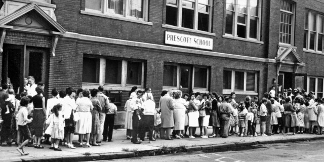 FILE - Parents and their children wait in long lines outside a Syracuse school to receive the Sabin oral polio vaccine on Aug. 29, 1961.