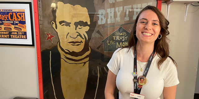 Lisa Errington, an assistant curator at the Ryman Auditorium, with a poster of Johnny Cash. One of the highlights of a tour of the auditorium is a visit to the Johnny and June Carter Cash dressing room.