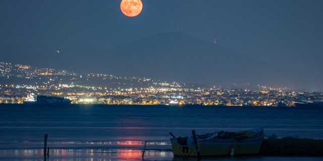 Lune avec lumières de la ville et bateaux de pêche locaux.  La pleine lune d'août Sturgeon se lève derrière le mont Hortiatis et la ville de Thessalonique au-dessus de la mer, et les observateurs du ciel l'appellent la lune bleue. 