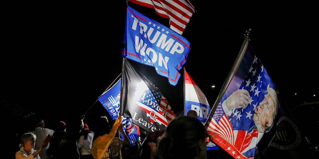 Сторонники бывшего президента США Дональда Трампа размахивают флагами, собравшись возле его дома в Мар-а-Лаго после того, как Трамп заявил, что агенты ФБР совершили налет на него, в Палм-Бич, Флорида, США, 8 августа 2022 года. 