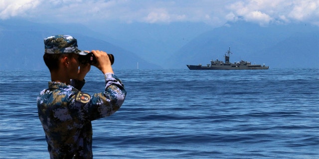 A People's Liberation Army member looks through binoculars during military exercises as Taiwan’s frigate Lan Yang is seen at the rear, on Friday, Aug. 5, 2022. China has repeatedly entered the waters and airspace of Taiwan in the past several weeks, Taiwan defense officials have said.
