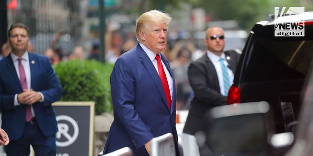 Donald Trump wearing a red tie and blue suit walking on the streets of New York City