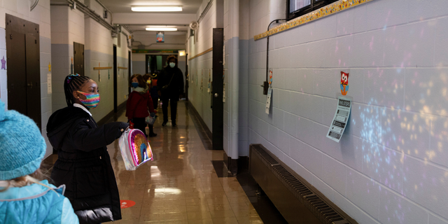 FILE - A student reflects her lunch bag on a wall in a hallway as COVID-19 restrictions are lifted in Philadelphia, March 8, 2021. 