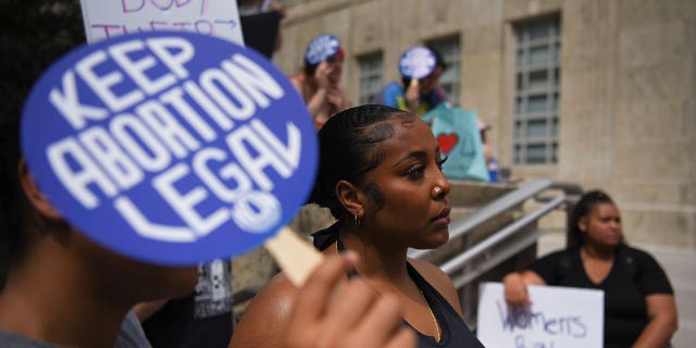 Pro-choice advocates stand outside with signs, one sign saying "Keep Abortion Legal"