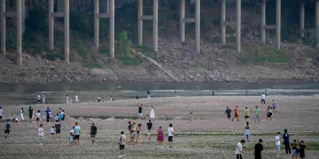 People walk along the dry riverbed of the Jialing River in southwestern China's Chongqing Municipality, on Aug. 20, 2022, after a prolonged drought caused the river to dry up.