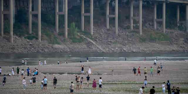 People walk along the dry riverbed of the Jialing River in southwestern China's Chongqing Municipality, on Aug. 20, 2022, after a prolonged drought caused the river to dry up.