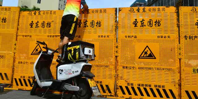 As China sticks to their strict "zero-COVID" policy, a delivery worker has to pass deliveries over a barrier of a locked down neighborhood in Sanya, Hainan province, China, on Aug. 6, 2022.