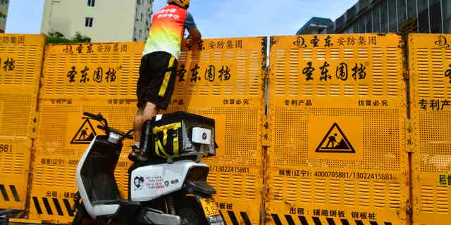 As China sticks to their strict "zero-COVID" policy, a delivery worker has to pass deliveries over a barrier of a locked down neighborhood in Sanya, Hainan province, China, on Aug. 6, 2022.