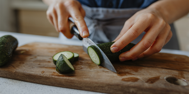 The Creamy Cucumber Tzatziki Salad recipe from midwesternhomelife.com calls for 1 English cucumber, thinly sliced. This stock image shows a person chopping up a cucumber.