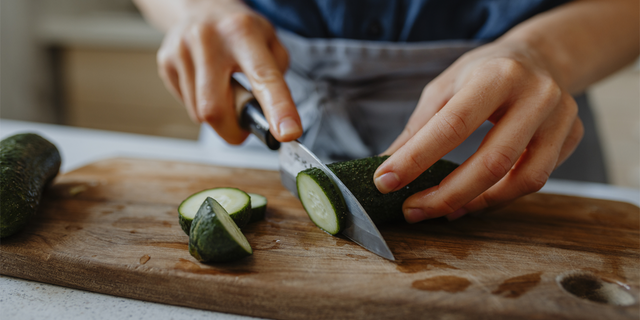 The Creamy Cucumber Tzatziki Salad recipe from midwesternhomelife.com calls for 1 English cucumber, thinly sliced. This stock image shows a person chopping up a cucumber.