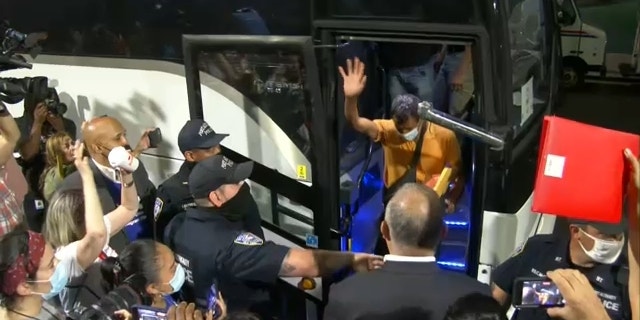 Migrants wave as they depart a bus in New York City from Texas.