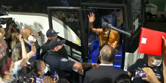 Migrants wave as they depart a bus in New York City from Texas.