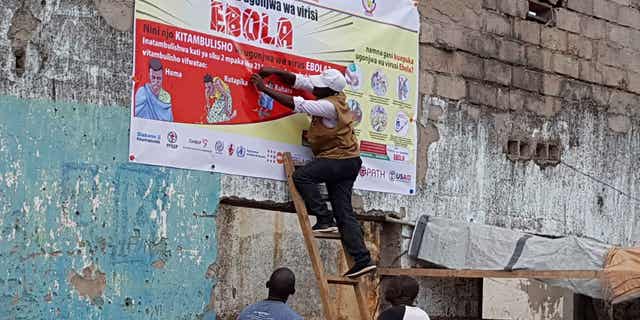 Regeneron's Inmazeb (REGN-EB3) monoclonal antibody medication, developed using the same rapid response technologies as Regeneron's COVID-19 medication, is one of the two drugs the WHO is now recommending to treat Ebola virus. Pictured: men resurrect Ebola awareness poster in Tchomia, Democratic Republic of Congo, on Oct. 9, 2018.