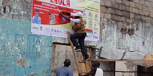 Regeneron's Inmazeb (REGN-EB3) monoclonal antibody medication, developed using the same rapid response technologies as Regeneron's COVID-19 medication, is one of the two drugs the WHO is now recommending to treat Ebola virus. Pictured: men resurrect Ebola awareness poster in Tchomia, Democratic Republic of Congo, on Oct. 9, 2018.