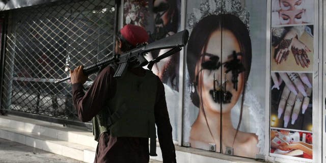 A Taliban fighter walks past a beauty salon with spray painted images of disfigured women in Shar-e-Naw in Kabul on August 18, 2021.