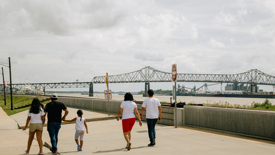 Photo shows a family walking in Baton Rouge with the Mississippi River Bridge in view 