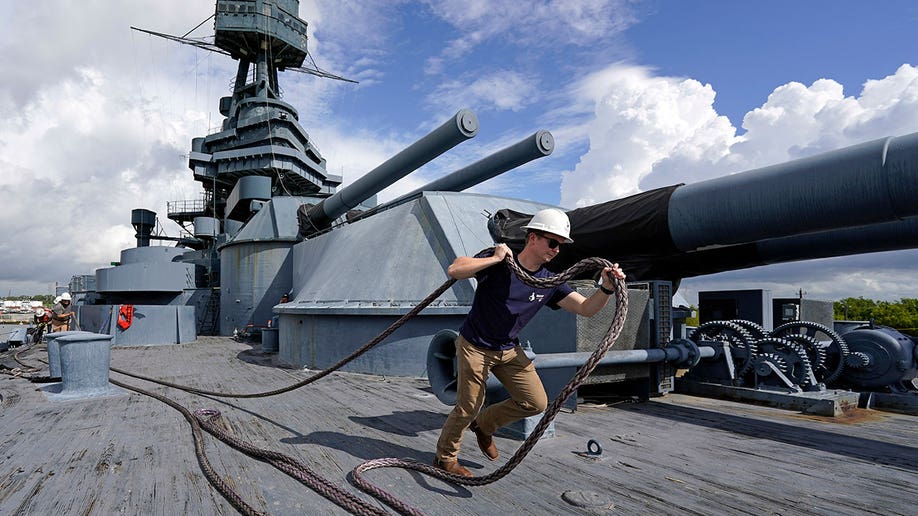 Man with a helmet carries a rope as he walks on the USS Texas during daytime