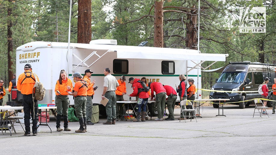 Kirely Rodni earch teams in bright jackets gather near an RV