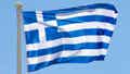 The Greek flag is photographed cast against a clear sky.