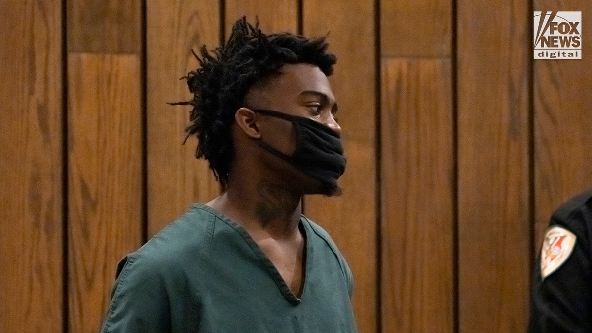 Ezekiel Kelly stands in court in green prison jumpsuit and black coronavirus mask