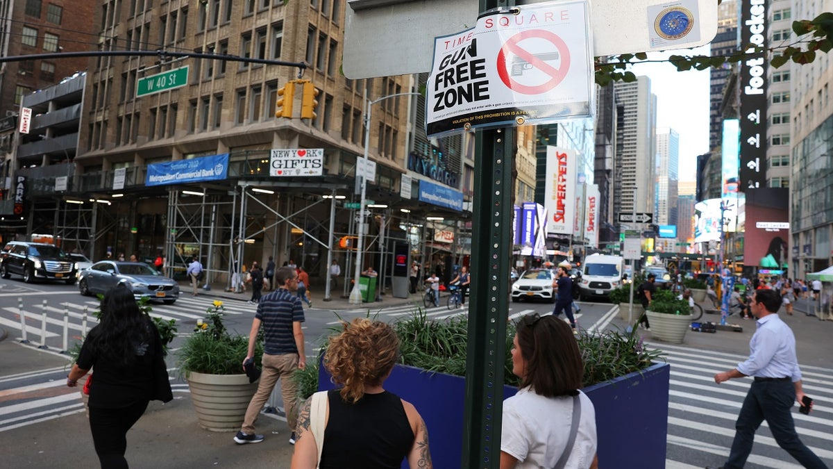 people walking past a sign that reads gun free zone