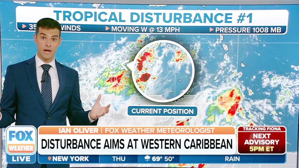 A weather reporter standing in front of a map showing a tropical disturbance