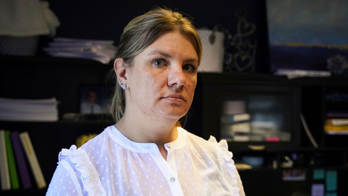 Aimee Bock está em frente a uma estante olhando para a câmera.