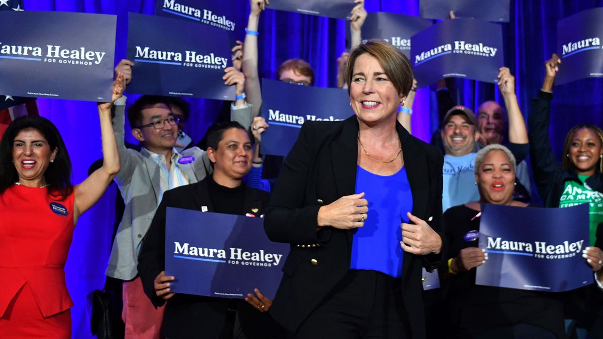 Maura Healey holding blazer in front of a crown and blue curtain.