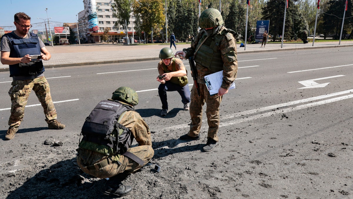 Investigators work at the site of a burning vehicle after shelling in Donetsk