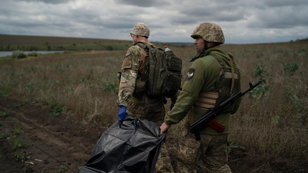 Ukrainian national guard servicemen carry a bag containing the body of a Ukrainian soldier in an area near the border with Russia, in Kharkiv region