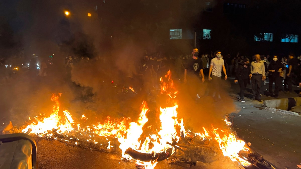 Iranian protesters gather around a burning police vehicle