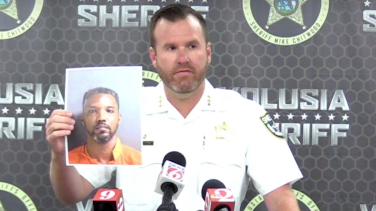 Brian Henderson holds up a booking photo of Michael Williams at a press conference.