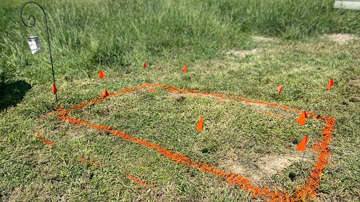 Outline of possible casket drawn in orange paint on grass