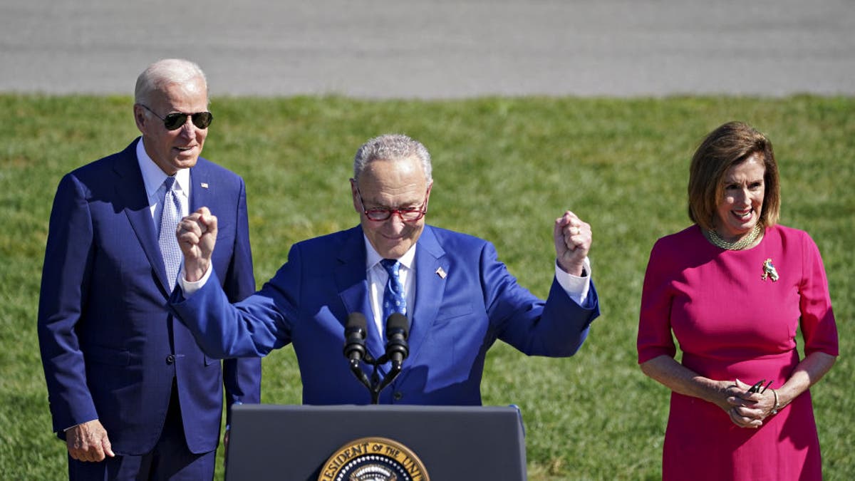 Chuck Schumer and Joe Biden in blue suits with Nancy Pelosi in pink at a signing ceremony