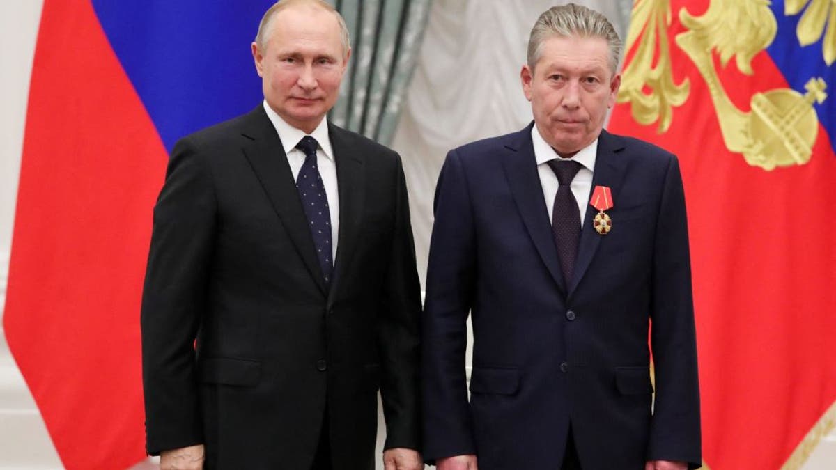 Vladimir Putin and Ravil Maganov in suits in front of a Russian flag