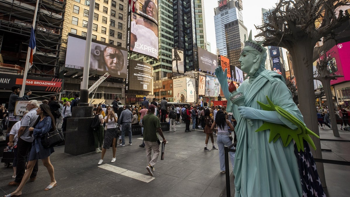 A costumed character stands in times square dressed like the statue of liberty