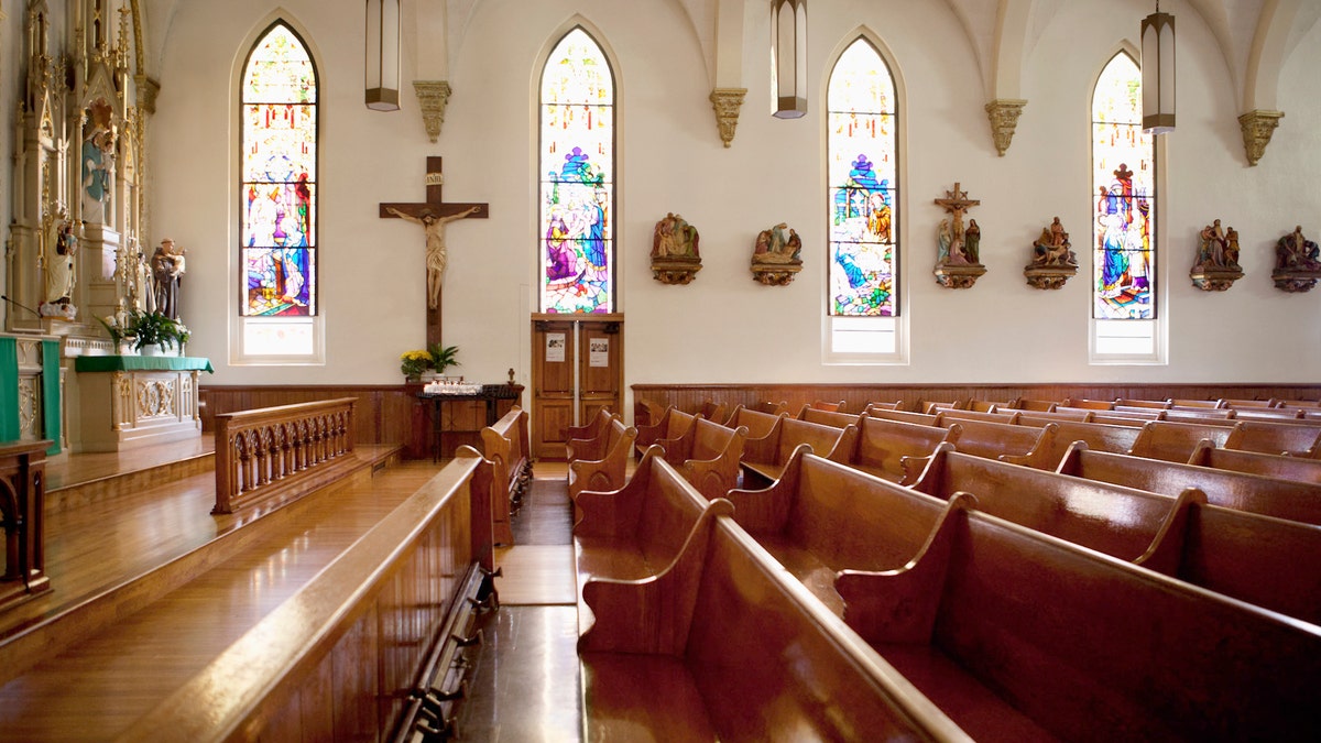 A church with stained glass windows stands empty church pews