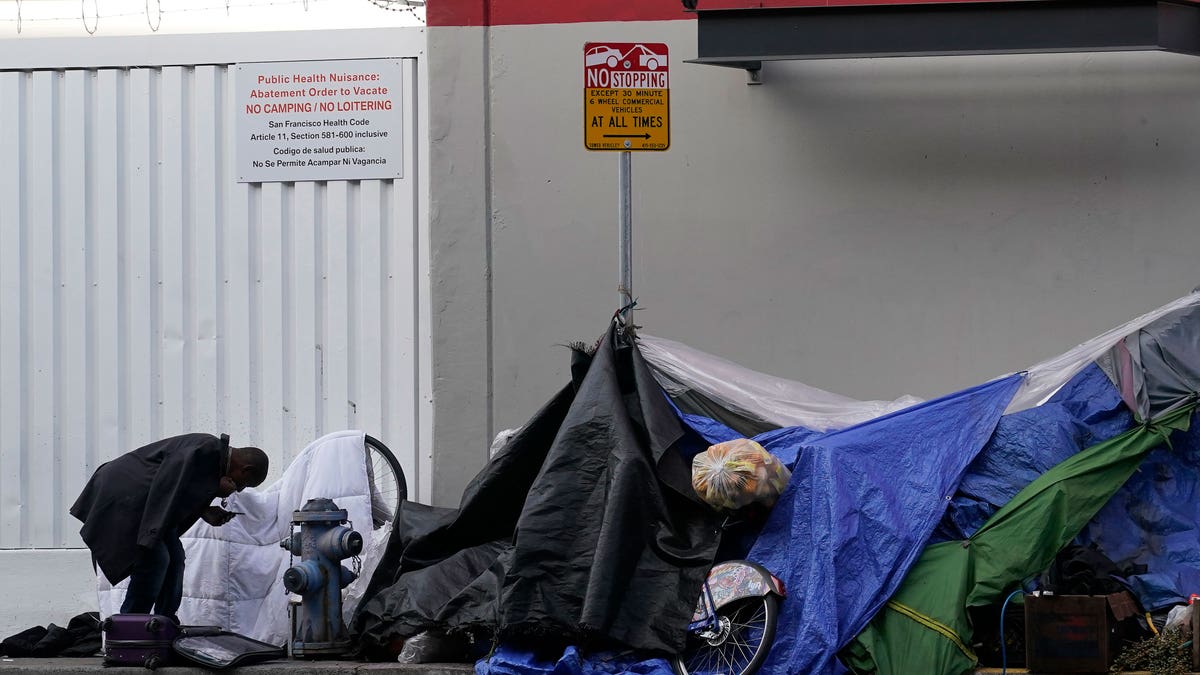 Homeless man standing next to tents on the street